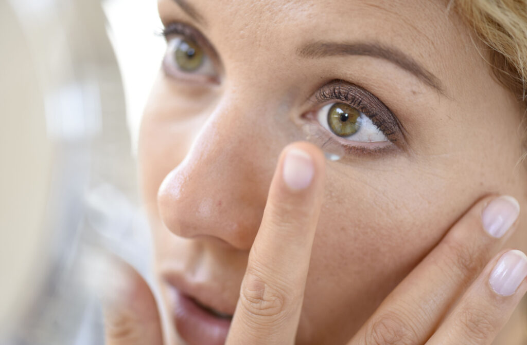 A close-up of a woman using a mirror to put her contact lens into her left eye.