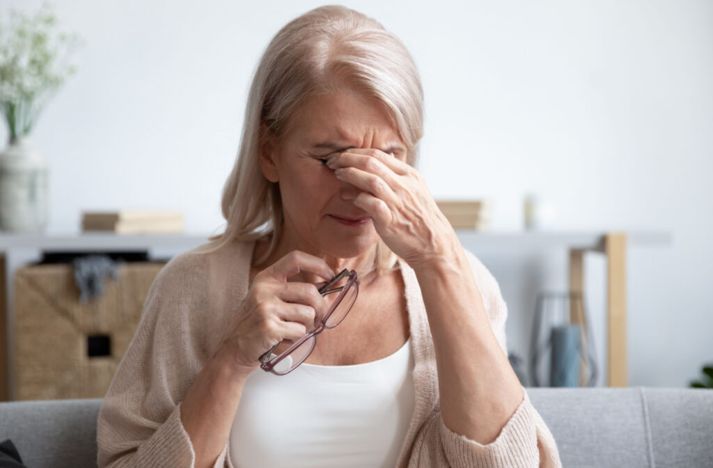 A woman holding glasses rubs her dry eyes